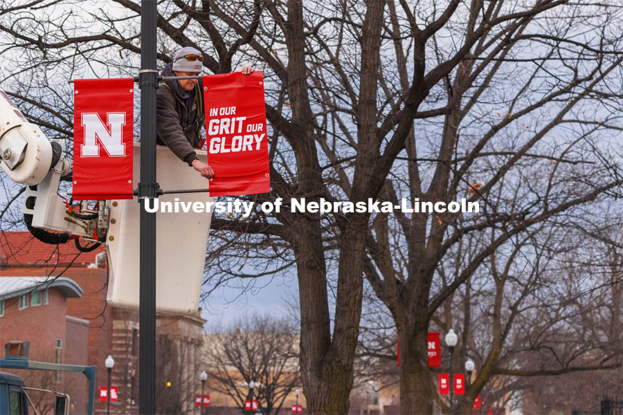 Drew Ehrisman, Construction Supervisor with Landscape Services, slides one of the new banners onto a light post. New banners are going up around campus. The N150 banners are being replaced by ones with our N and Go Big Red, alternating with In Our Grit Our Glory. March 25, 2021. Photo by Craig Chandler / University Communication.