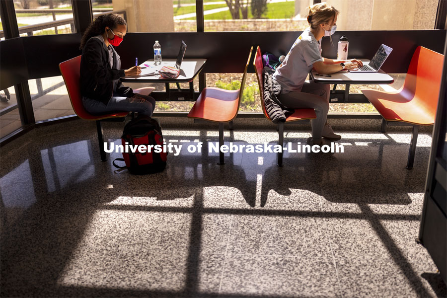 Gabriella Silva (red mask) and Zoe Keese (white mask) study at the tables in the sun lit lobby inside Hamilton Hall. March 30, 2021. Photo by Craig Chandler / University Communication.