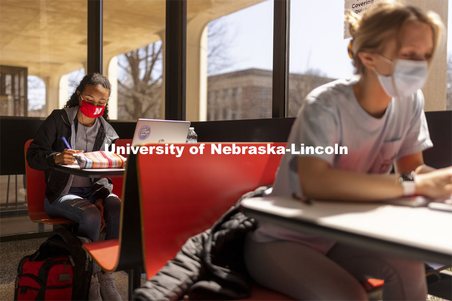 Gabriella Silva (red mask) and Zoe Keese (white mask) study at the tables in the sun lit lobby inside Hamilton Hall. March 30, 2021. Photo by Craig Chandler / University Communication.
