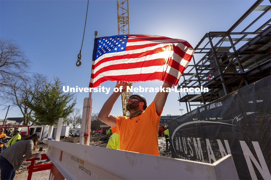 A Hausmann Construction employee unfurls a flag placed on the final steel beam during the topping out ceremony on April 9. The ceremony has roots to an ancient Scandinavian tradition that, in modern times, signals the completion of the internal structure of a building. Topping out ceremony for the new construction atop the demolished Mabel Lee Hall. April 9, 2021. Photo by Craig Chandler / University Communication.