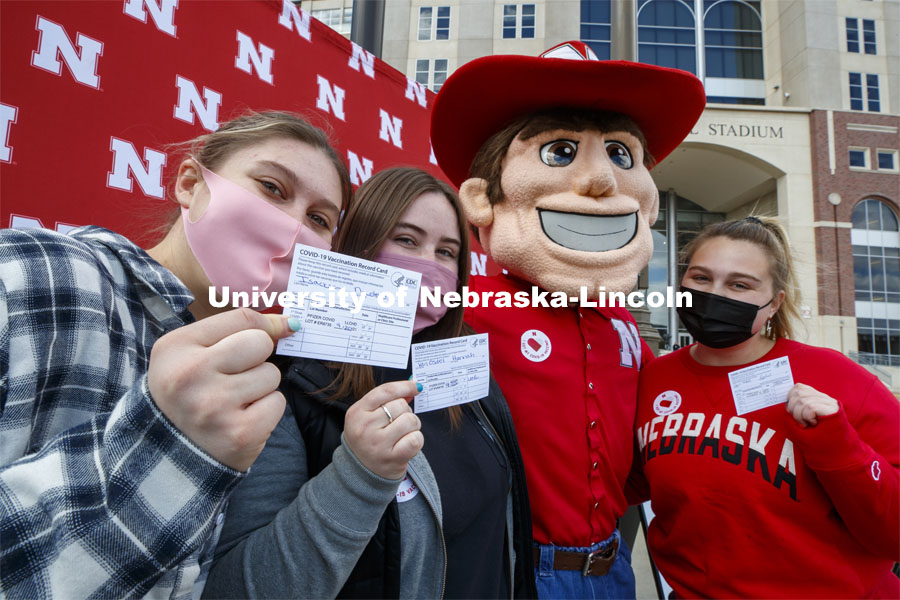 Huskers show off their vaccine cards with Herbie Husker at the after-vaccine party in the parking lot of East Stadium. Vaccine clinic in the Coliseum with a free food and goodies tent outside. April 20, 2021. Photo by Craig Chandler / University Communication.  