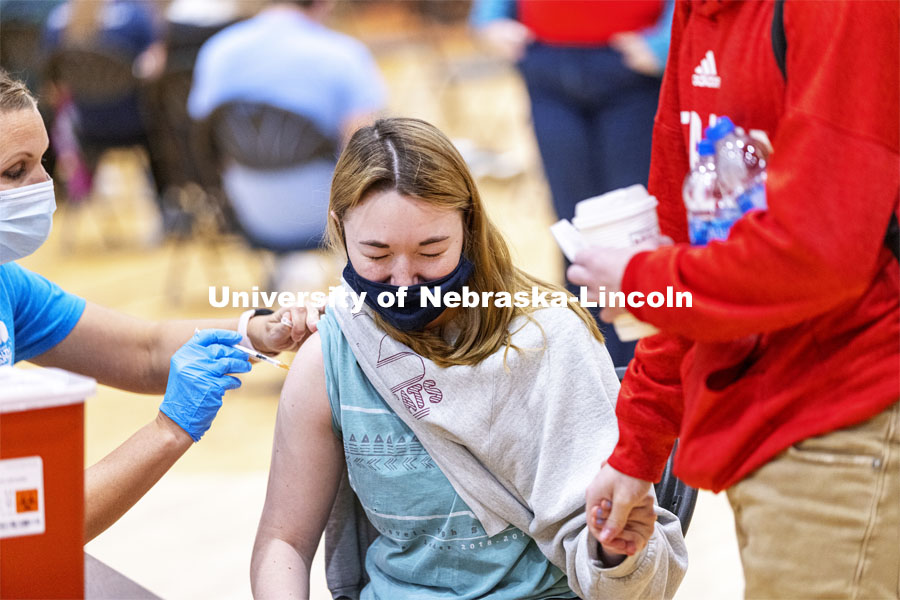 Emily Kuhl holds hands with Jacob Eckert for moral support as she receives her first dose of vaccine during a COVID-19 vaccination clinic April 20 at the Coliseum. She did say it didn’t hurt. Vaccine clinic in the Coliseum with a free food and goodies tent outside. April 20, 2021. Photo by Craig Chandler / University Communication.
