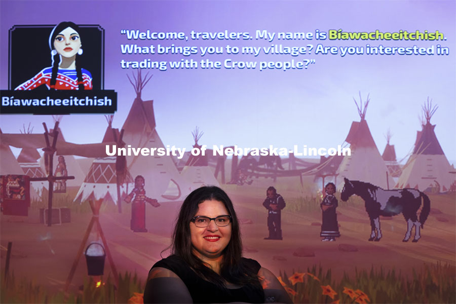 Margaret Huettl, Assistant Professor in History and Ethnic Studies, poses in front of a screen shot of the redesigned Oregon Trail game. Huettl consulted in the redesign. The redesign was to bring the game up to modern standards and root out historical inaccuracies and cliches about Native American culture. Huettl has Lac Courte Oreilles tribal ancestors. She researched old photos and drawings for accurate depictions of different tribes’ clothing and style. May 21, 2021. Photo by Craig Chandler / University Communication.  