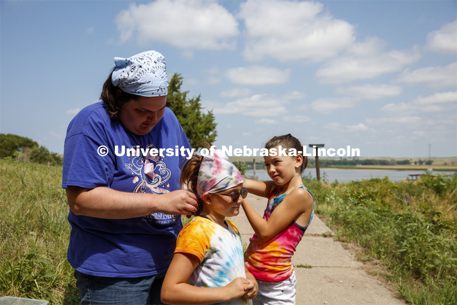 A staff member helps a young camper tie her newly tie dyed scarf around her head. Cedar Point Biological Station near Ogallala, Nebraska. July 19, 2021. Photo by Annie Albin / University Communication.