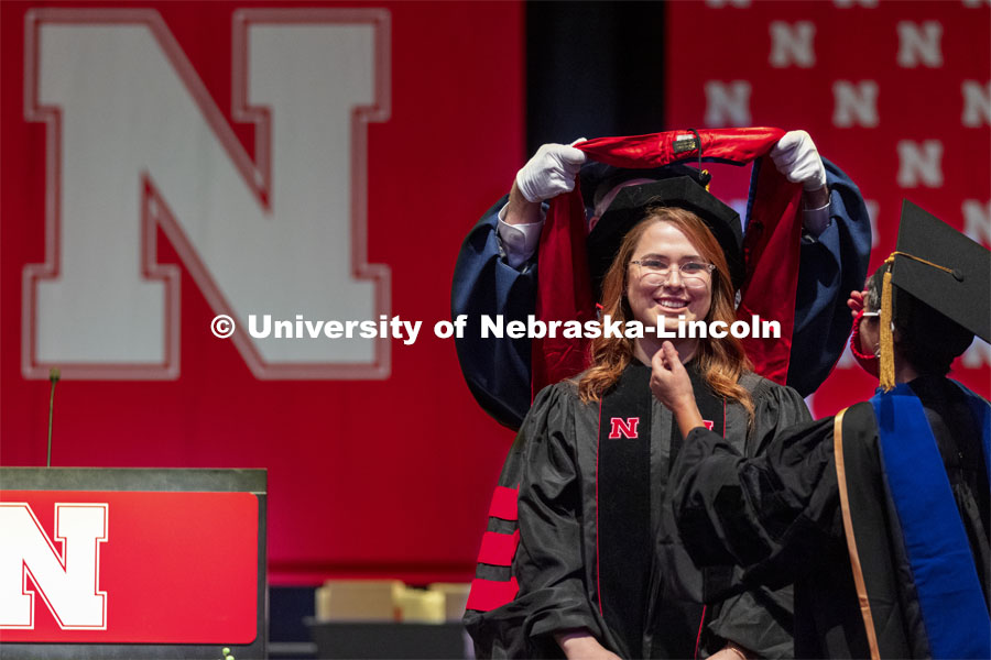 First generation college student and now a doctor in human sciences Ashley Mulcahy Toney smiles as her hood is placed over her. Summer Graduate Commencement at Pinnacle Bank Arena. August 13, 2021. Photo by Craig Chandler / University Communication.