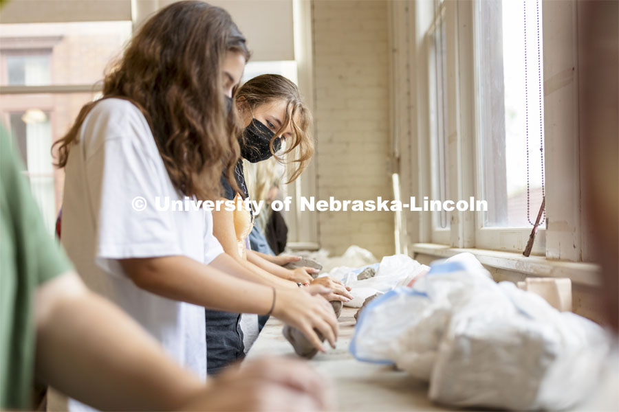Jena Nelson, a sophomore from Omaha, looks over to a classmate as they wedge lumps of clay in the beginning wheel class. First day of classes for fall semester. August 23, 2021. Photo by Craig Chandler / University Communication.