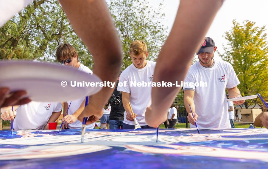 Riley Berner, a senior from Norfolk, is framed by fellow painters working on “Lift Off”. Lift Off is an entrepreneurial community mural painting in the green space outside the Nebraska Union. The student-created design will be hung in the College of Business. September 1, 2021. Photo by Craig Chandler / University Communication.