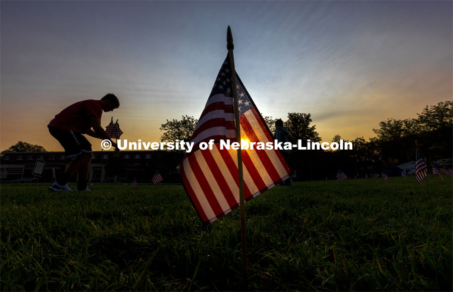 Dylan Jensen, a freshman from Columbus, Nebraska, sets up flags in the green space north of the Nebraska Union to commemorate 9/11. Jensen said his dad has been on active duty for 22 years and has deployed twice to Iraq and once to Bosnia. He said his dad lost a good friend in Bosnia in 2003 and Dylan said he has seen what the loss has meant to his dad. Putting out he flags is his way to honor his dad and all who lost their lives on 9/11 and in the war. 9/11 memorials. September 9, 2021. Photo by Craig Chandler / University Communication.