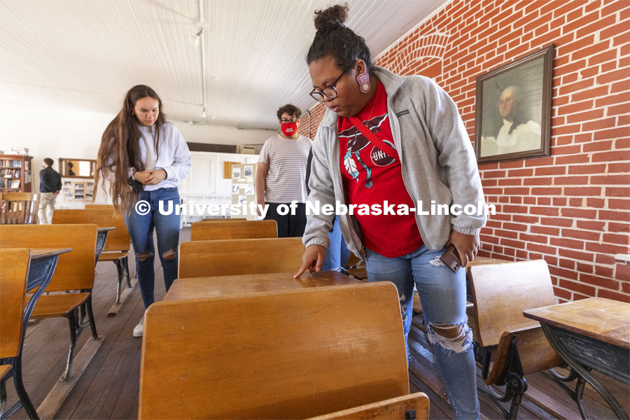 Nasia Olson-Whitefeather runs her finger along a student’s name scratched into the old desks saved from the school. Students from UNITE tour the Genoa Indian School in Genoa, Nebraska. October 10, 2021. Photo by Craig Chandler / University Communication.