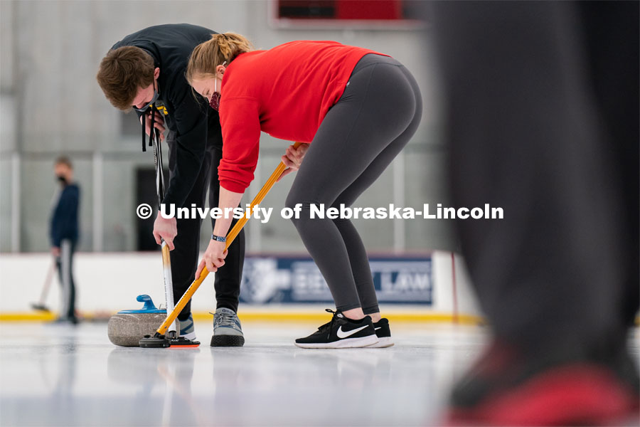 Seamus Hurley (left) and Olivia Schuster (right) sweep a curling stone during practice at the John Breslow Ice Hockey Center. Curling Club. February 1, 2022. Photo by Jordan Opp for University Communication.