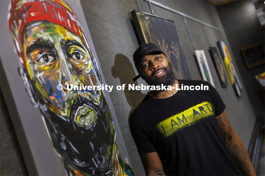 Jevon Woods poses next to a self-portrait entitled “Jevon”. Woods is a Black artist from Lincoln whose work is on display in the loft gallery at the East Campus Union through this month as part of Black History Month. February 9, 2022. Photo by Craig Chandler / University Communication.