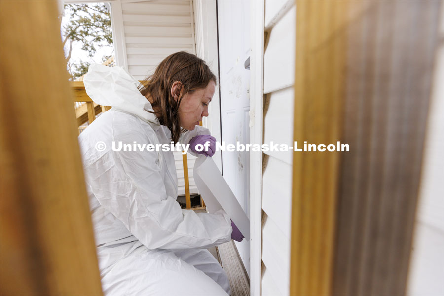 Michaela Andrusko applies a sticky sheet to the door of the house to capture a dirty handprint for evidence. Students do crime scene investigation in the murder house. Forensic Science “Murder House” is a small derelict house on the north side of East Campus that has been rebuilt and made accessible for students to use as a location forensic lab. February 17, 2022. Photo by Craig Chandler / University Communication.