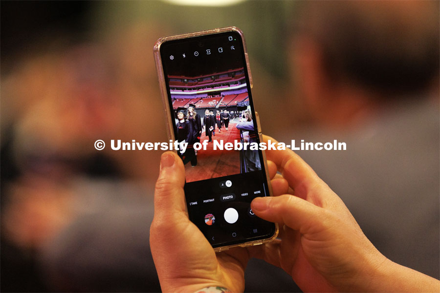 A family member snaps a photo on their phone of their grad marching in for commencement. Graduate commencement in Pinnacle Bank Arena. May 13, 2022. Photo by Craig Chandler / University Communication.