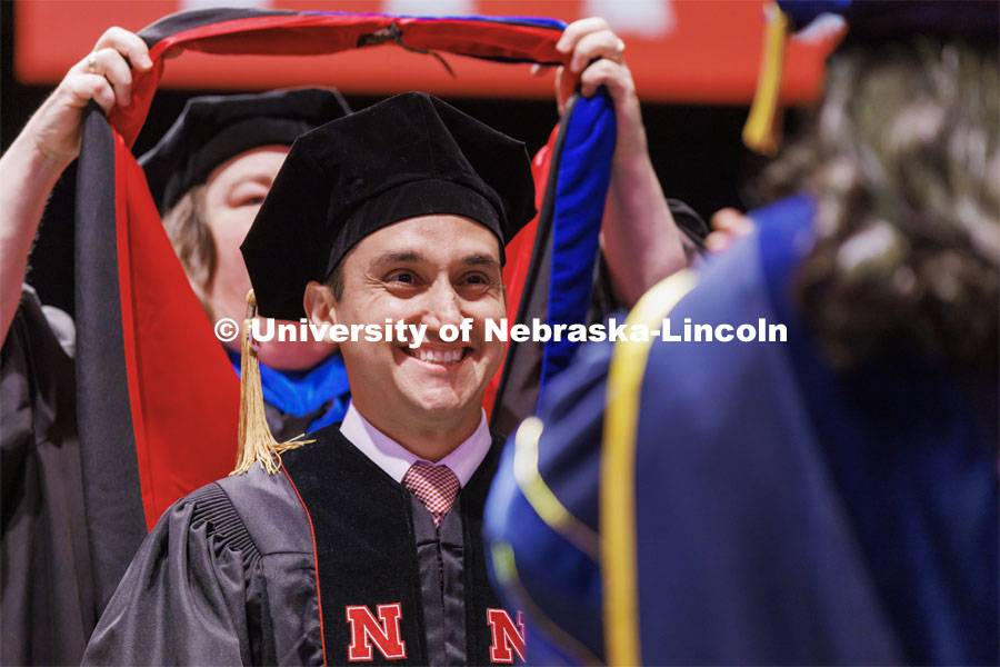Moises Padilla smiles as his doctoral hood is lowered over his head. Graduate commencement in Pinnacle Bank Arena. May 13, 2022. Photo by Craig Chandler / University Communication.