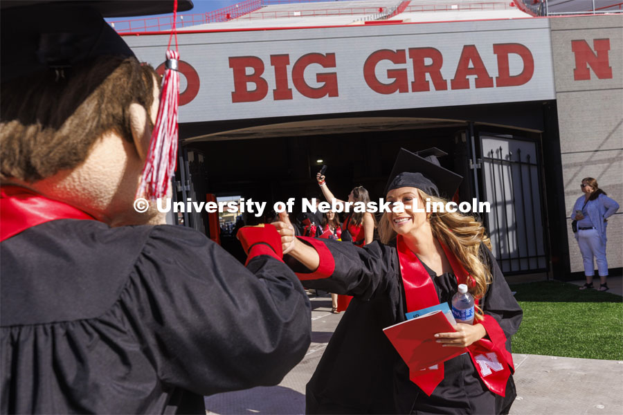 A graduate is greeted by Herbie Husker with a fist-bump. UNL undergraduate commencement in Memorial Stadium. May 14, 2022. Photo by Craig Chandler / University Communication.