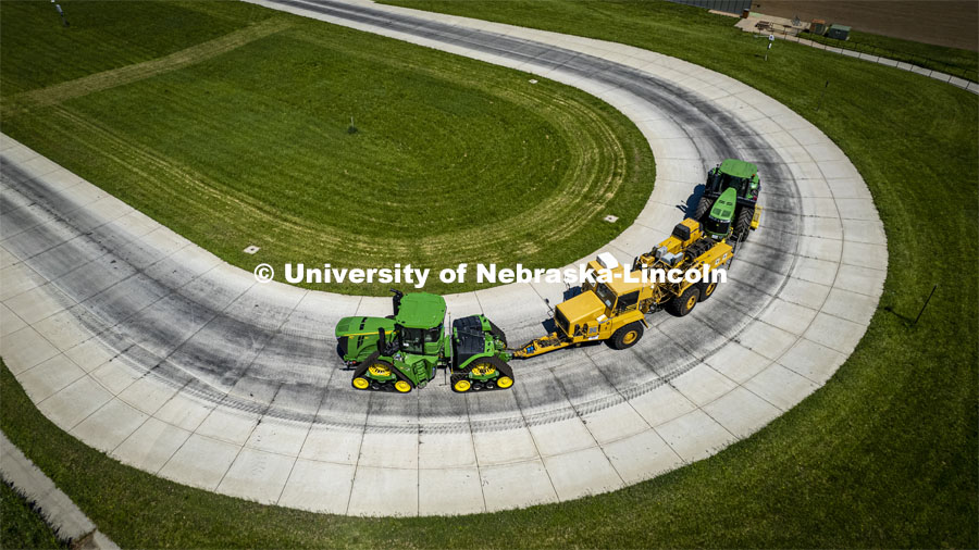 High angle view of a tractor as it pulls the test car (yellow) and an additional tractor for weight as it rounds the test track on east campus. The University of Nebraska Tractor Test Laboratory (NTTL) is the officially designated tractor testing station for the United States. It has operated for more than 100 years. East Campus. May 27, 2022. Photo by Craig Chandler / University Communication.