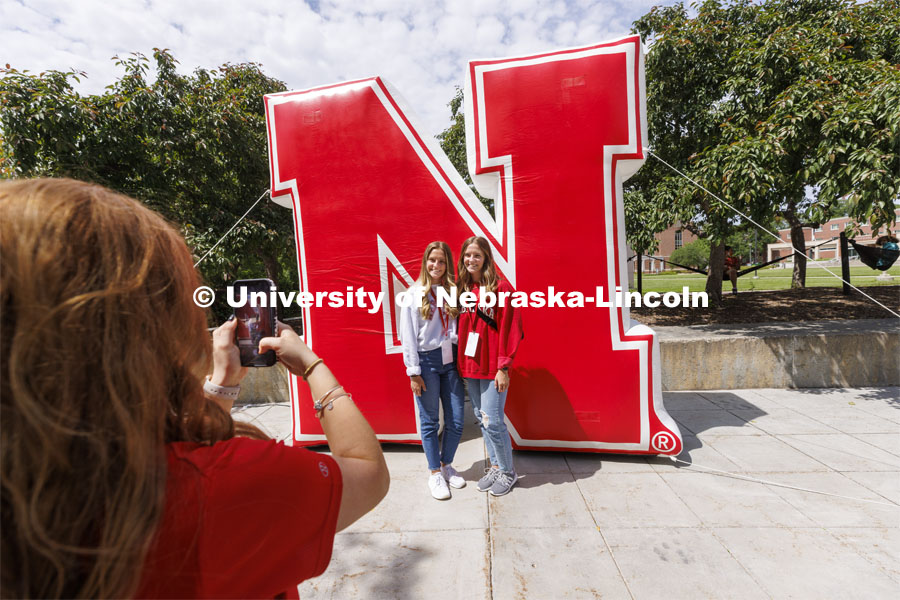 Grace and Emma Alder, twin sisters from Atkinson, NE, pose for NSE Leader Hannah-Kate Kinney in front of an inflatable N sculpture on the Union Plaza. New Student Enrollment. June 1, 2022. Photo by Craig Chandler / University Communication.