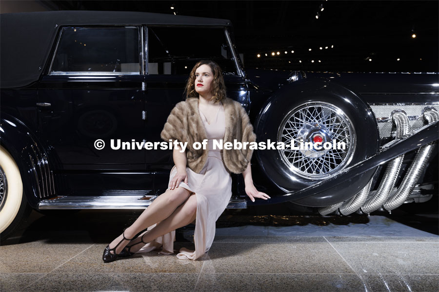 Anna Kuhlman evokes Hollywood glamour in a ’30s-style gown, featuring bias-cut panels and flowing sleeves in a soft pink. Paired with a vintage fur stole and T-strap heels, she poses next to a 1930 Duesenberg Model J at the Speedway Motors Museum of Speed. Kuhlman, who earned her master’s degree in May, researched fashion of the 1930s. June 7, 2022. Photo by Craig Chandler / University Communication.
