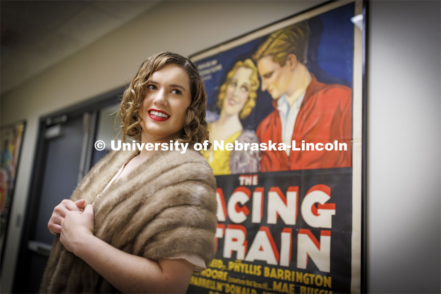 Anna Kuhlman poses in front of a poster for Racing Strain, a 1932 racing movie. Kuhlman, who earned her master’s degree in May, researched fashion of the 1930s. June 7, 2022. Photo by Craig Chandler / University Communication.