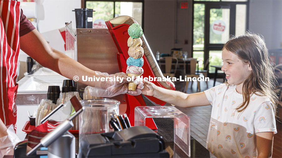 Randy Nguyen serves up a cone of colorful ice cream to Allie Wiesman, 9. She and her parents are visiting from Kentucky. Ice cream is scooped up at the Dairy Store on East Campus. July 18, 2022. Photo by Craig Chandler / University Communication.