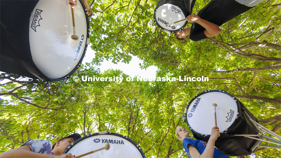 The Cornhusker Marching Band percussion groups kick off the school year. Bass drummers, clockwise from upper right, Carter Ross, Abby Reasoner, Peyton Comer and Alaric Schiltz, practice in the shade outside the Lied Center. Drum line practice on the first day of Cornhusker Marching Band camp. August 11, 2022. Photo by Craig Chandler / University Communication.