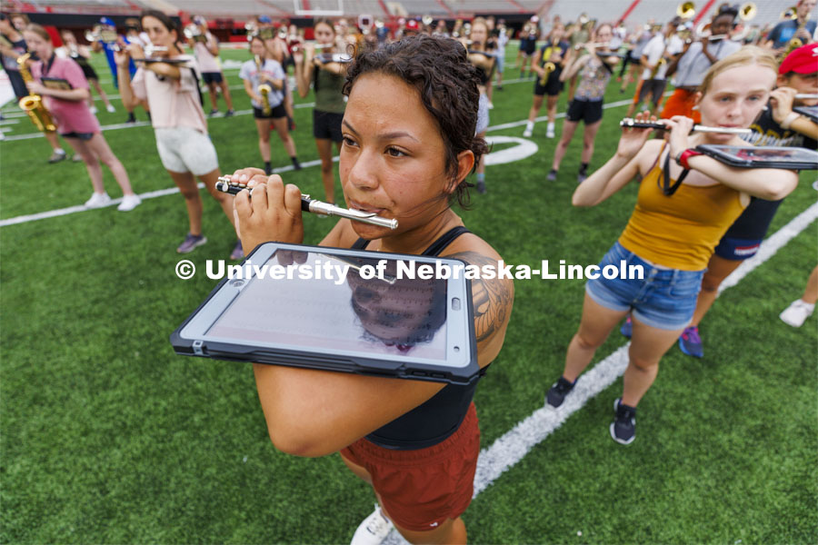 Vivika Ortiz uses an iPad balanced on her arm to keep track of her music and choreography along with other band members during practice in Memorial Stadium under the lights. August 18, 2022. Photo by Craig Chandler / University Communication.