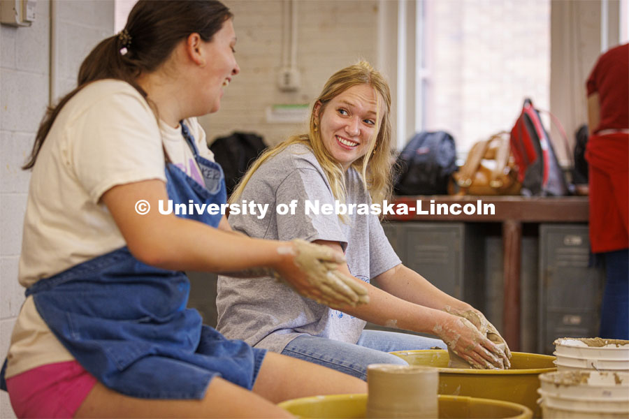 Sophie Hellebusch, right, a senior from Marthasville, Missouri, laughs with Kally Karkazis, a senior from Western Springs, Illinois, as they discuss their first attempts at wheel throwing in Richards Hall. Students in wheel throwing ceramics class. August 24, 2022. Photo by Craig Chandler / University Communication.