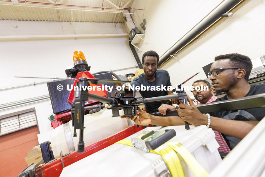 Herve Mwunguzi, Santosh Pitla and Terence Irumva discuss how a drone will be fitted to a robotic tractor to refill seed for planting. Santosh Pitla in his robotics lab on East Campus. September 2, 2022. Photo by Craig Chandler / University Communication.