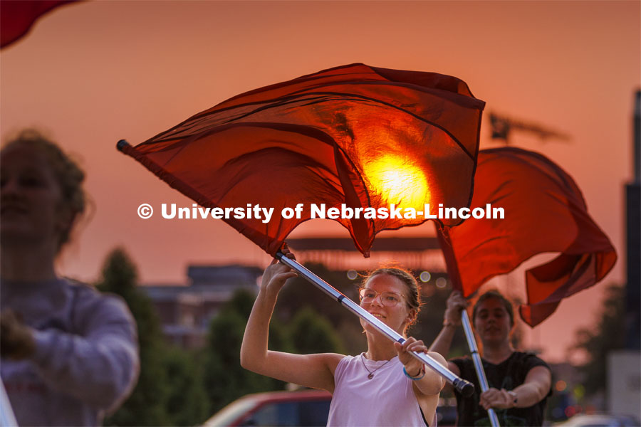 The rising sun appears to burn a hole through the flag of Cornhusker Marching Band color guard member Jaedynn Shively, a sophomore from Lincoln. Campus sunrise. September 8, 2022. Photo by Craig Chandler / University Communication.