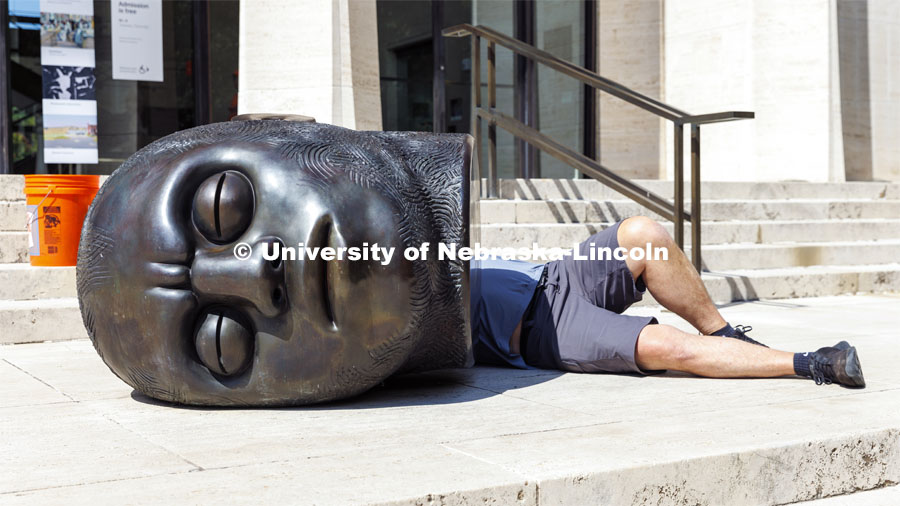 Big head, little body. Rob Jensen of Jensen Conservation of Omaha lays behind the Fallen Dreamer sculpture outside the Sheldon as he applies a coat of wax to the sculpture. September 15, 2022. Photo by Craig Chandler / University Communication.