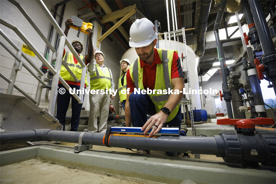 Andrew Hansen, graduate student in Environmental Engineering, uses an ultrasonic water flow meter to obtain a water flow rate as in the background Bruce Dvorak, center, Professor of Civil and Environmental Engineering, coaches Yves Cedric Tamwo Noubissi, left, senior in Mechanical Engineering, and Sussan Moussavi, graduate student in Civil Engineering, in the use of a Fluke Precision Acoustic Imager used to detect leaks of gases and vacuum from pipes and tanks. They are working inside Lincoln’s Theresa Street Wastewater Treatment Plant. September 23, 2022. Photo by Craig Chandler / University Communication.