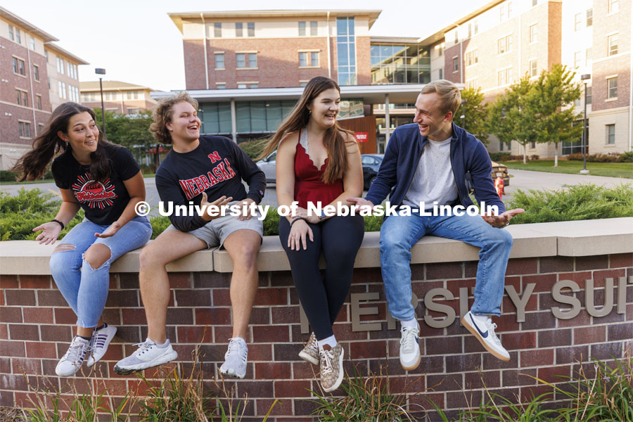 Students seated on a brick wall outside of University Suites Residence Hall. Housing Photo Shoot in University Suites Residence Hall. September 27, 2022. Photo by Craig Chandler / University Communication.