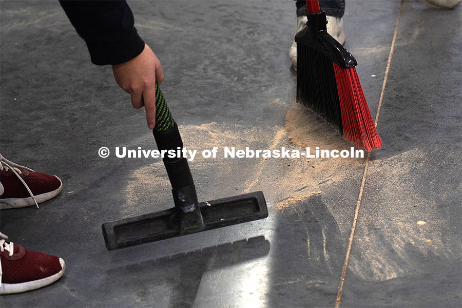 Students clean up the saw dust in the shop. Architecture design professor Aziza Cyamani is doing a weekend long furniture design-build sprint with Professor Chris Martin from Iowa State University. The students will come Friday, Saturday and Sunday and make something out of wood and another version using a new technology like 3D printing. October 30, 2022. Photo by Kirk Rangel for University Communication.