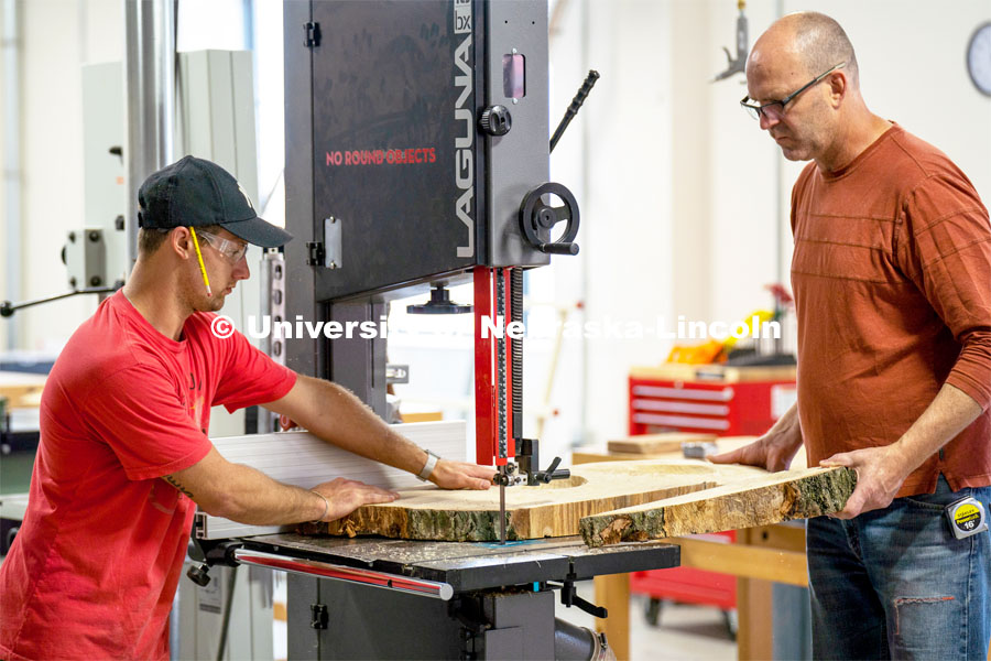 Iowa State professor Chris Martin, right, helps student Thomas Gerees as he cuts his project with the band saw. Architecture design professor Aziza Cyamani is doing a weekend long furniture design-build sprint with Professor Chris Martin from Iowa State University. The students will come Friday, Saturday and Sunday and make something out of wood and another version using a new technology like 3D printing. October 30, 2022. Photo by Kirk Rangel for University Communication.