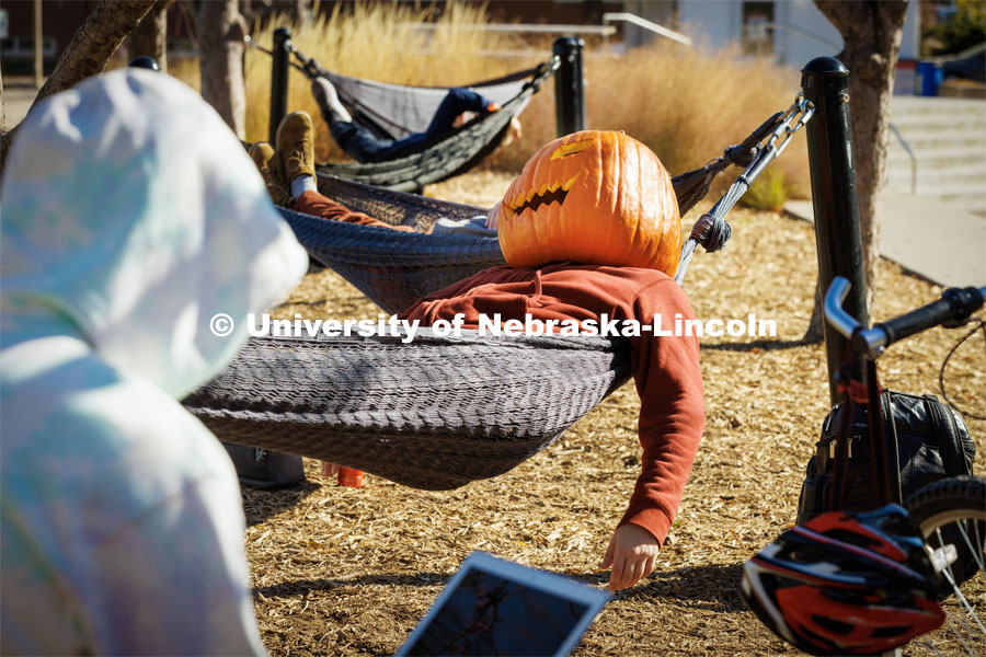 Andrejs Sedriks, a second-year student from Lincoln, takes a break in the hammocks outside the Nebraska Union. Sedriks said the head, carved from an actual pumpkin was pretty heavy but after the first few minutes didn’t really smell pumpkiny any longer. Halloween on City Campus. October 31, 2022. Photo by Craig Chandler / University Communication.
