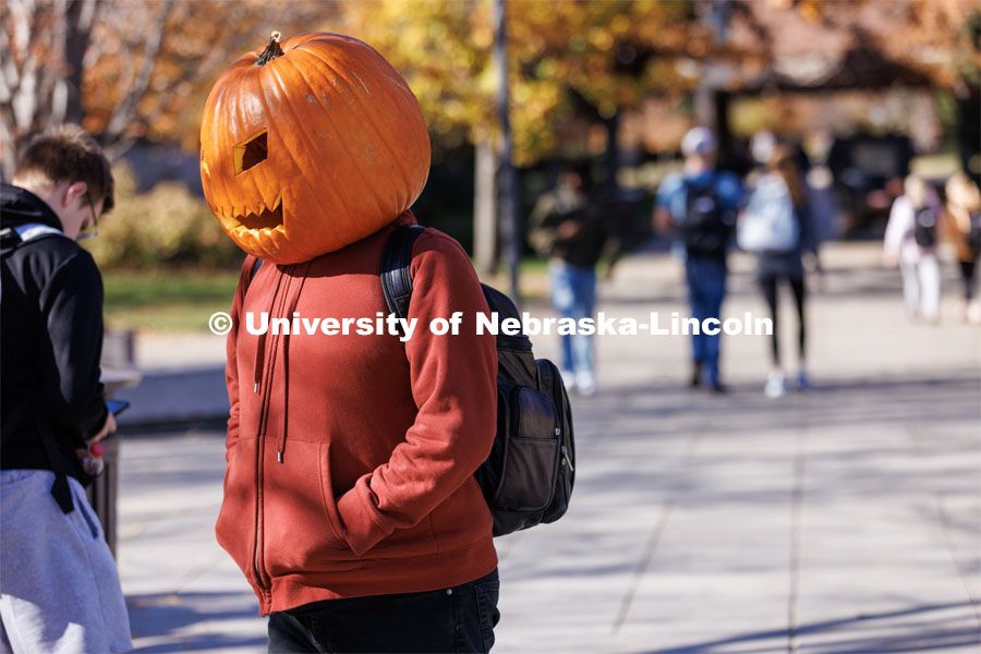 Andrejs Sedriks, a second-year student from Lincoln, walks across the plaza at the Nebraska Union wearing a carved pumpkin. Sedriks said the head, carved from an actual pumpkin was pretty heavy but after the first few minutes didn’t really smell pumpkiny any longer. Halloween on City Campus. October 31, 2022. Photo by Craig Chandler / University Communication.