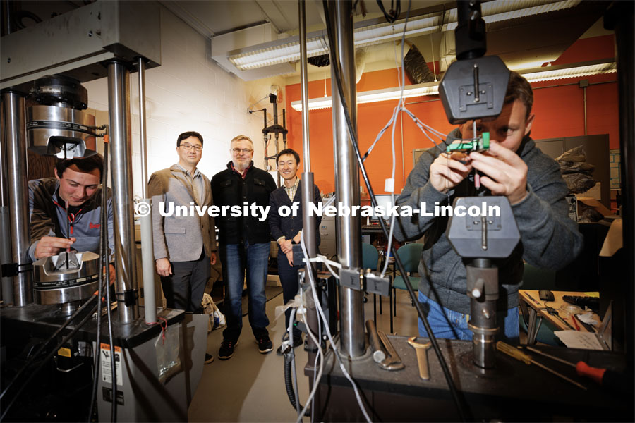 Husker Engineers Jongwan Eun (center left), Yuris Dzenis (center) and Seunghee Kim (center right) pose in Dzenis’ lab as Benjamin Bashtovoi (left), a junior mechanical engineering major, and Mikhail Kartashov (right), an engineering graduate student, test carbon-fiber samples. Eun, Dzenis and Kim have received $675,000 from the Department of Energy’s Established Program to Stimulate Competitive Research to investigate how inorganic microfibers can make a more resilient barrier material to improve the long-term storage capabilities of vessels that contain high-level nuclear waste and spent nuclear fuel (SNF). November 14, 2022. Photo by Craig Chandler / University Communication.