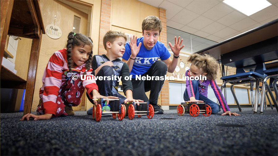 Spencer Knight gets three students and their rubber-band powered cars lined up for a race. Nebraska honors students Spencer Knight (blue shirt) and Rohan Tatineni (glasses) work with Riley Elementary students in their after-school STEM club. November 22, 2022. Photo by Craig Chandler / University Communication.
