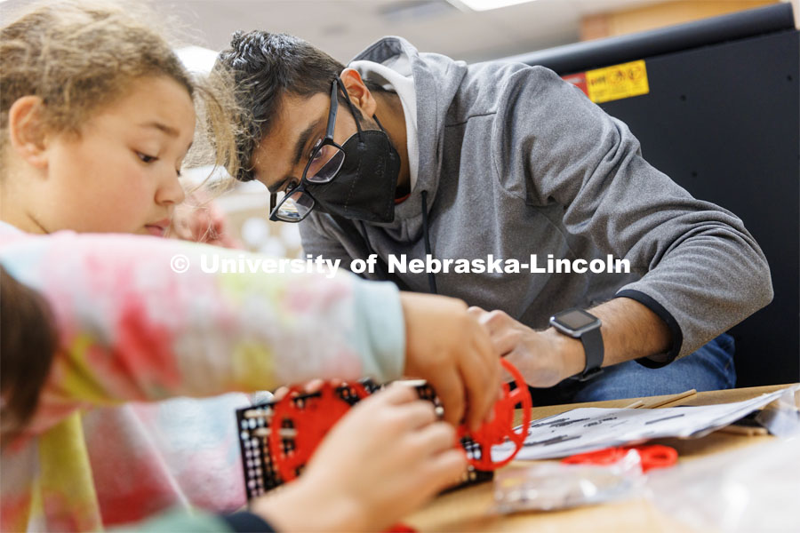 Rohan Tatineni helps a student build her rubber-band powered car. Nebraska honors students Spencer Knight (blue shirt) and Rohan Tatineni (glasses) work with Riley Elementary students in their after-school STEM club. November 22, 2022. Photo by Craig Chandler / University Communication.