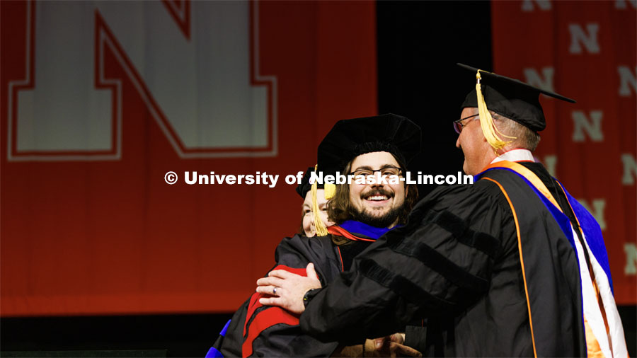 Nate Korth smiles to friends and family as he is congratulated by Andy Benson on his doctoral degree. Graduate Commencement in Pinnacle Bank Arena. December 16, 2022. Photo by Craig Chandler / University Communication.