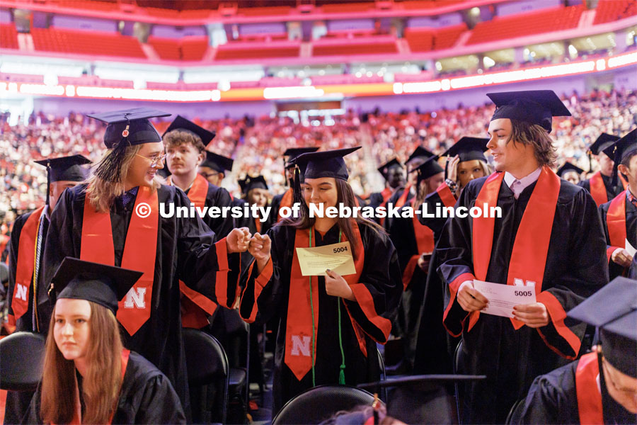 Journalism graduates Carson Allen, Carmella Bailey and Thomas Baker, left, fist bump to celebrate the college’s graduates being called to the stage. Winter Undergraduate Commencement in Pinnacle Bank Arena. December 17, 2022. Photo by Craig Chandler / University Communication.