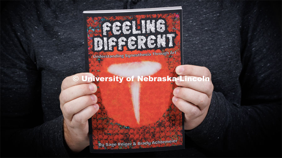Reiger holds a copy of the book he co-authored, "Feeling Different." Sage Reiger, a videographer/editor with Nebraska Public Media, has synesthesia and his brain processes music as colors. He has produced artwork to show what he hears and written a book about his experiences. December 19, 2022. Photo by Craig Chandler / University Communication.
