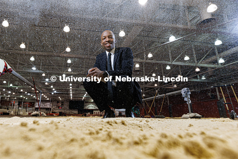 Nebraska's Passmore Mudundulu kneels at the edge of the jump pit in the Devaney Sports Center as sand rains down in front of the camera. Mudundulu is a junior marketing major from Lincoln. Photo for Black History Month profile. February 10, 2023. Photo by Craig Chandler / University Communication.