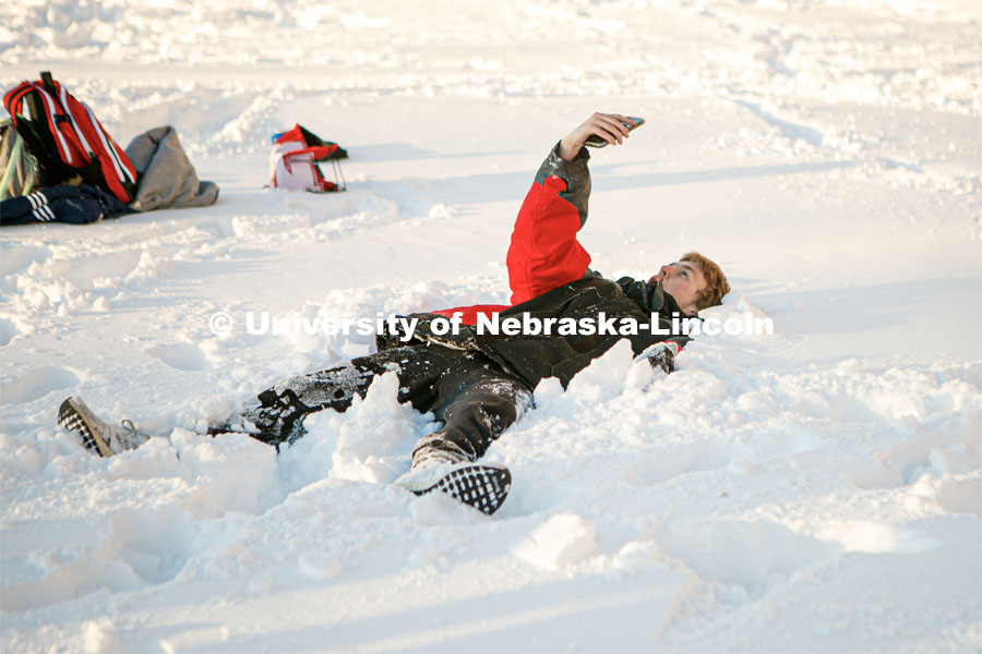A student lays in the snow to take his BeReal on Thursday during a snow volleyball match outside the Harper Schramm Smith residence halls. Snow volleyball. February 16, 2023. Photo by Sammy Smith for University Communication.