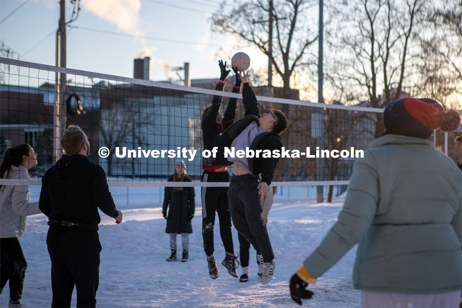 Two students meet at the net to hit the ball while playing volleyball with a big group of friends Thursday outside the Harper Schramm Smith residence halls. Snow volleyball. February 16, 2023. Photo by Sammy Smith for University Communication.