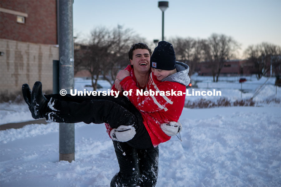 Two friends jump in each others arms while their friends play volleyball in the snow on Thursday outside the Harper Schramm Smith residence halls.  Feb. 16, 2023. Photo by Sammy Smith for University Communication