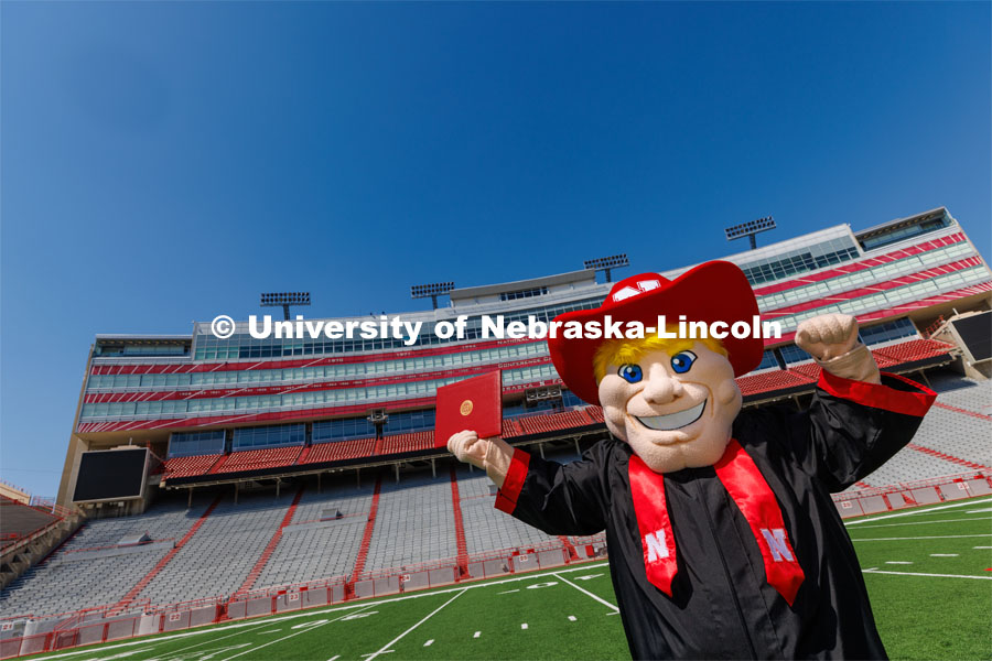 Herbie poses on the field in Memorial Stadium in his graduation regalia. New Herbie photoshoot. April 7, 2023. Photo by Craig Chandler / University Communication.