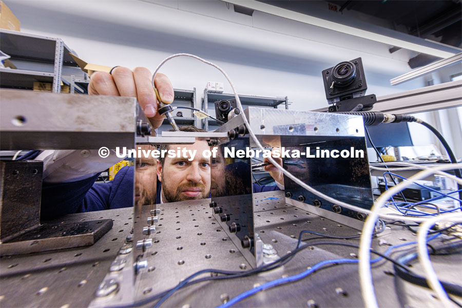 Keegan Moore, Assistant Professor of Mechanical and Materials Engineering, places a bolt into a flexible structure so vibrations can be measured which cause the bolt to loosen. He uses high speed cameras (background) capable of 30,000 frames a second to record the vibrations. Moore is a 2023 CAREER winner. May 12, 2023. Photo by Craig Chandler / University Communication.