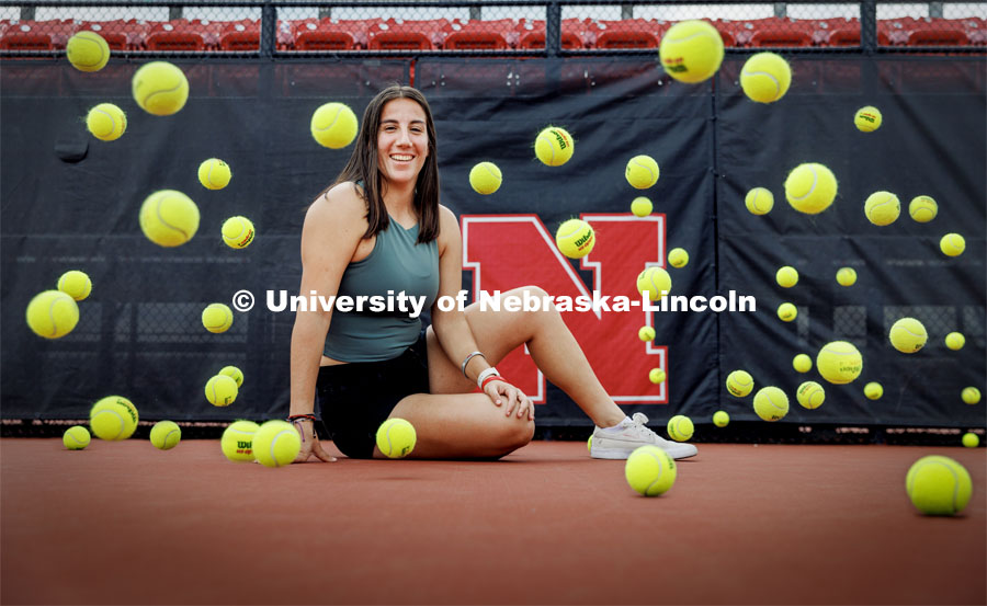 Tennis balls bounce around Isabel Adrover Gallego as she poses for a photo on the tennis court. Gallego, a senior in computer engineering and a Husker tennis player from Mallorca, Spain. Photo for Pride Month profile. May 18, 2023. Photo by Craig Chandler / University Communication.
