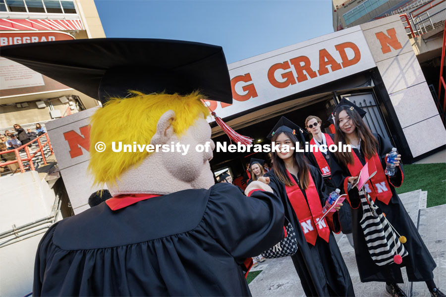 Herbie offers up a fist bump to grads as they enter the field. Undergraduate commencement at Memorial Stadium. May 20, 2023. Photo by Craig Chandler / University Communication.